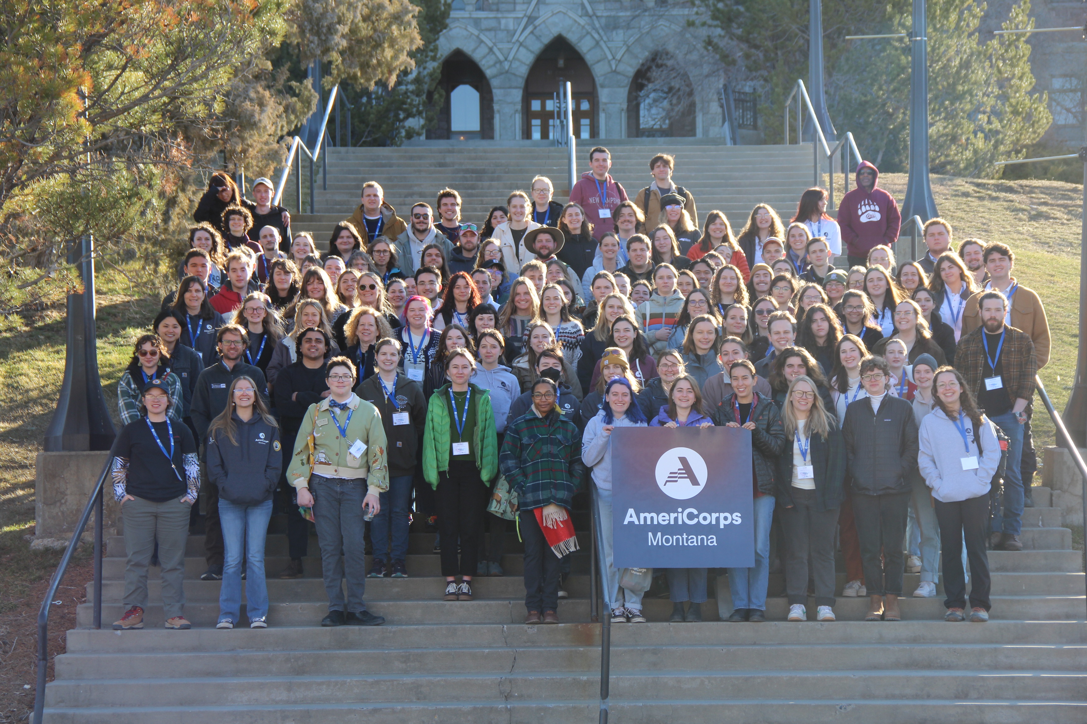 large group of individuals standing on staircase holding AmeriCorps logo
